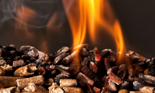 Close-up of wood pellets burning, with vibrant orange flames and glowing embers creating a warm, fiery glow.