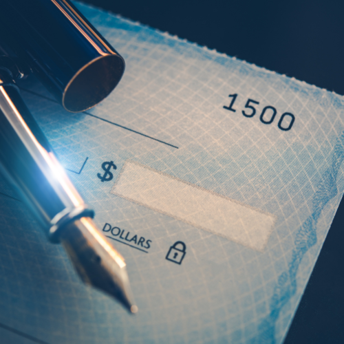An unwritten check with a pen resting on it. The check is blue with a pattern of small white lines and has the check number 1500.